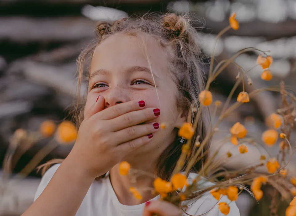 Flo lacht achter haar hand, met een bosje gele bloemen op haar communiedag