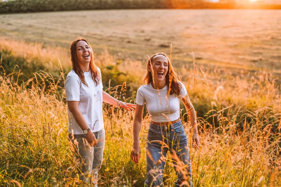 Twee zussen lachen samen in het hoge gras in het avondlicht