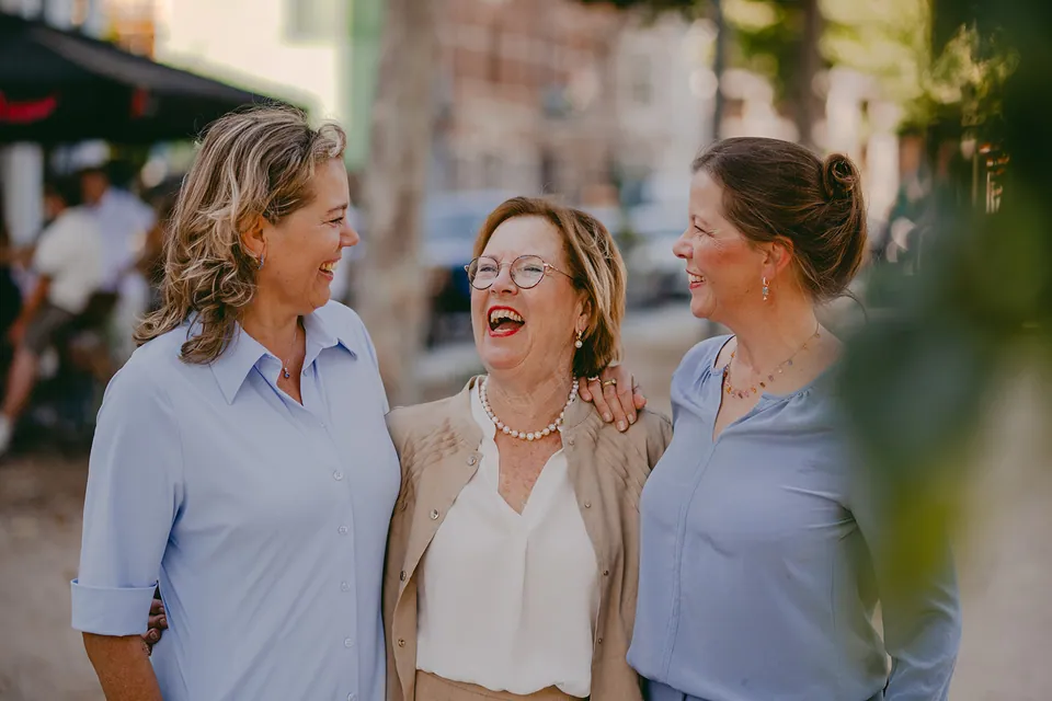 Drie vrouwen in lichtblauw, wit en zand lachen samen in de stad