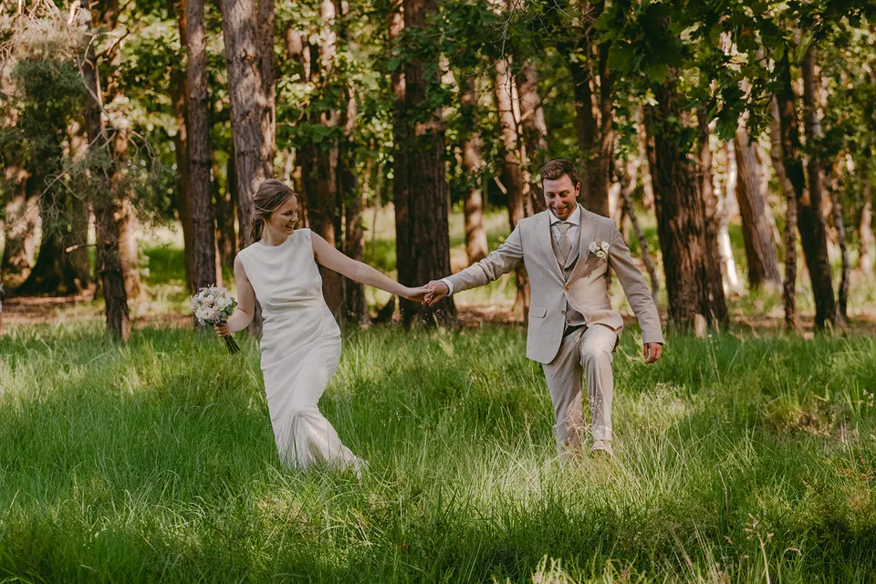 Bruidspaar huppelt hand in hand door het hoge gras